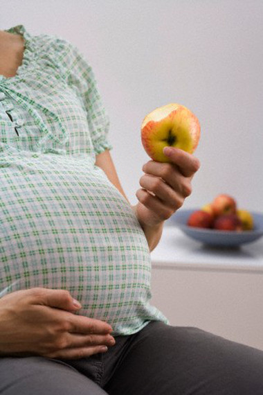 A pregnant woman eating an apple, midsection